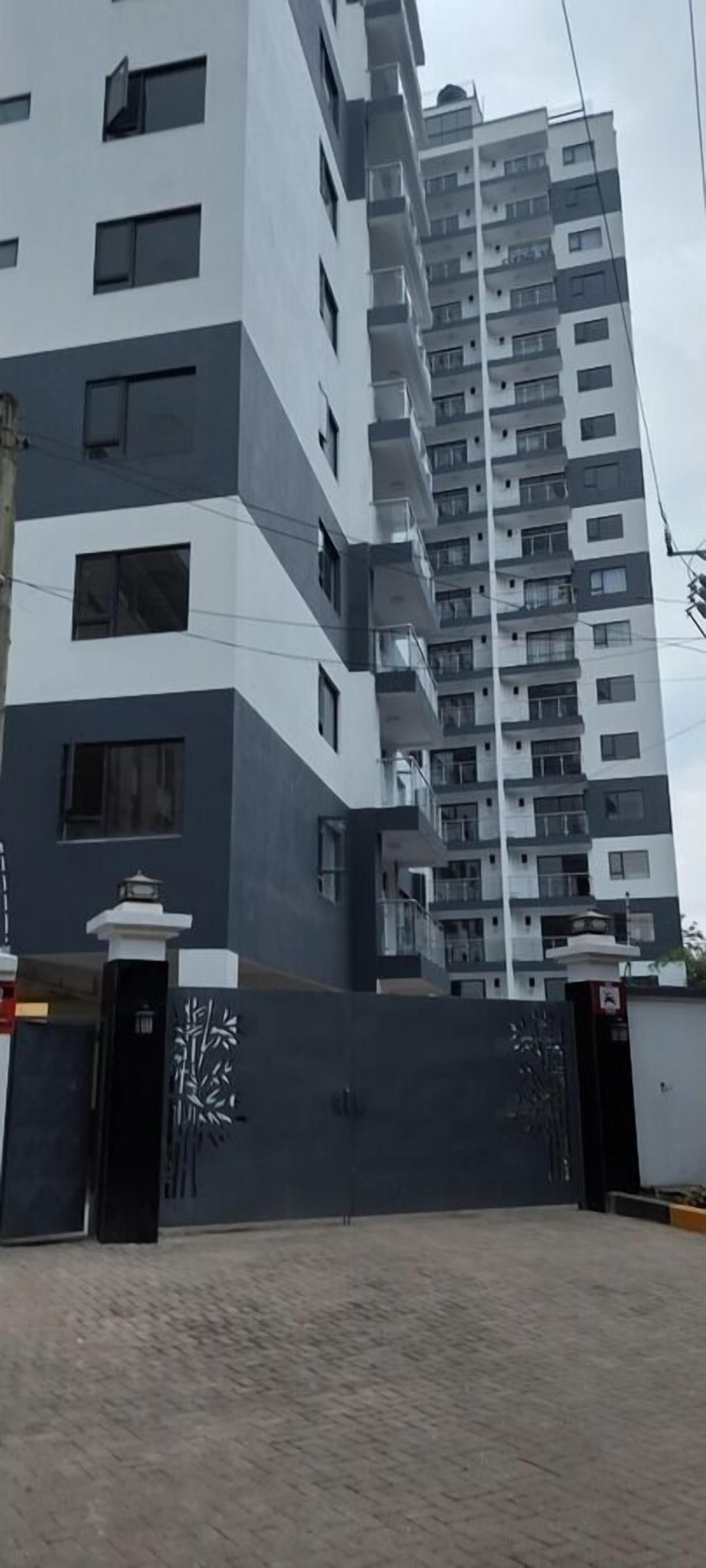 A modern multi-story residential building with a gated entrance and a landscaped area in front.