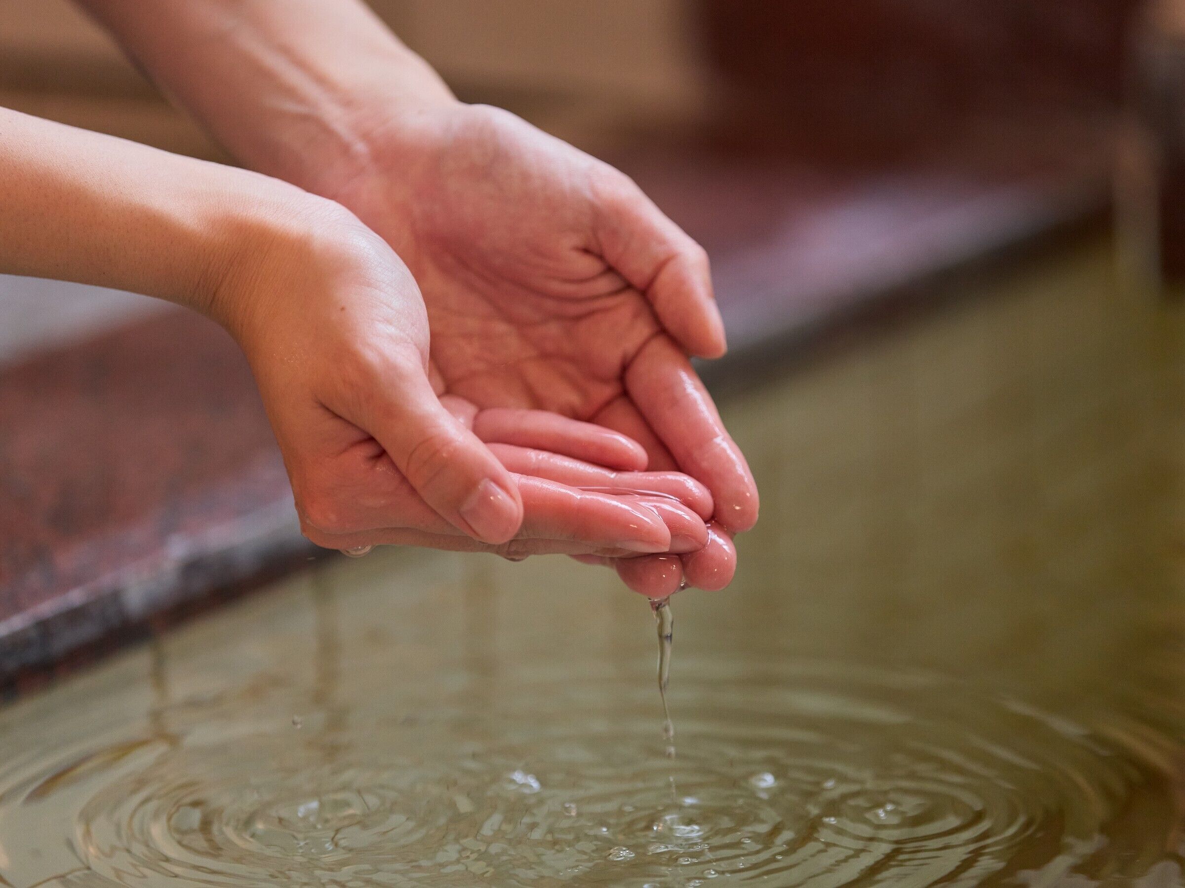 Hands cupping water from a tap, with ripples forming on the surface.