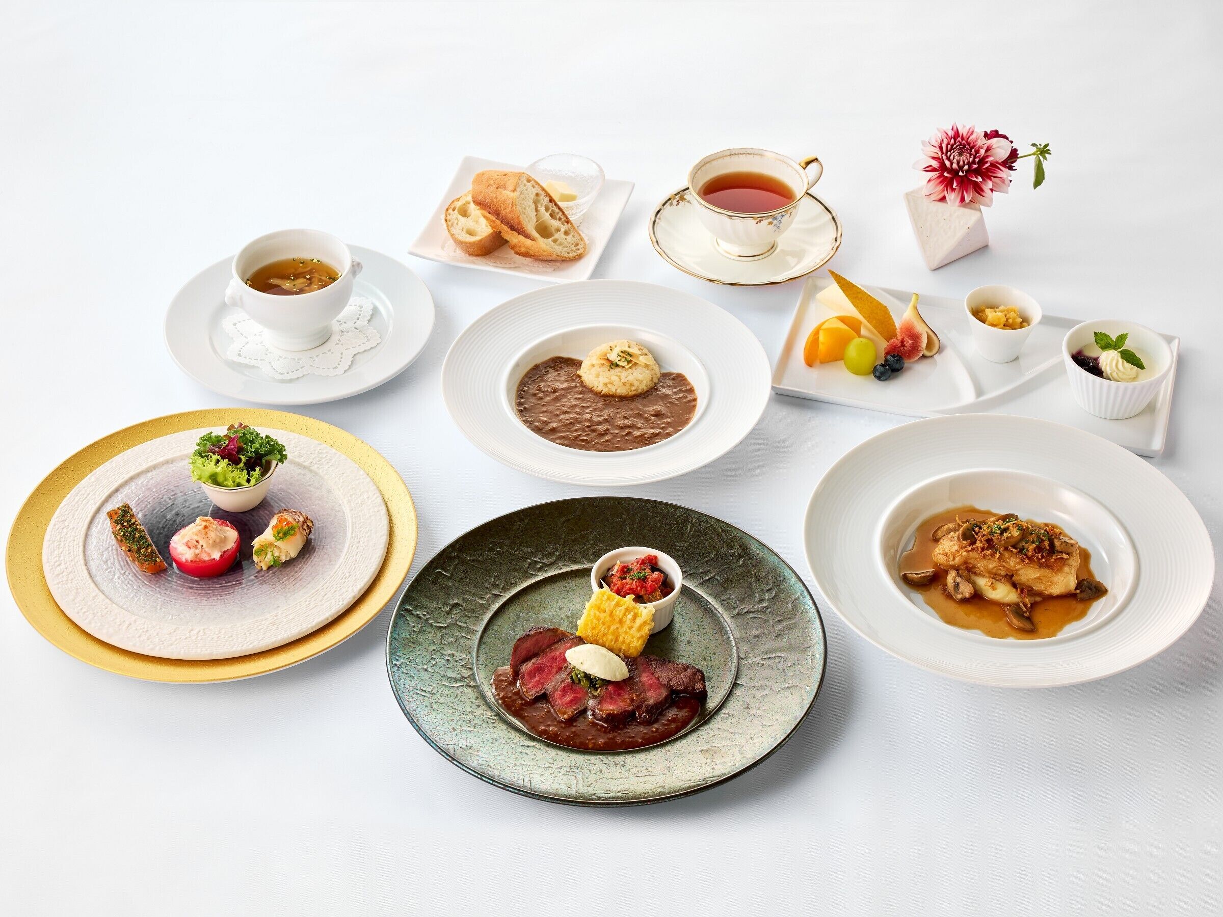 A variety of dishes including a salad, soup, and meat, arranged on different plates and bowls.
