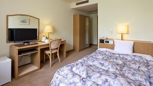 Une chambre d’hôtel comprenant un lit, un bureau avec un ordinateur, une chaise, une télévision et une table de chevet avec une lampe.