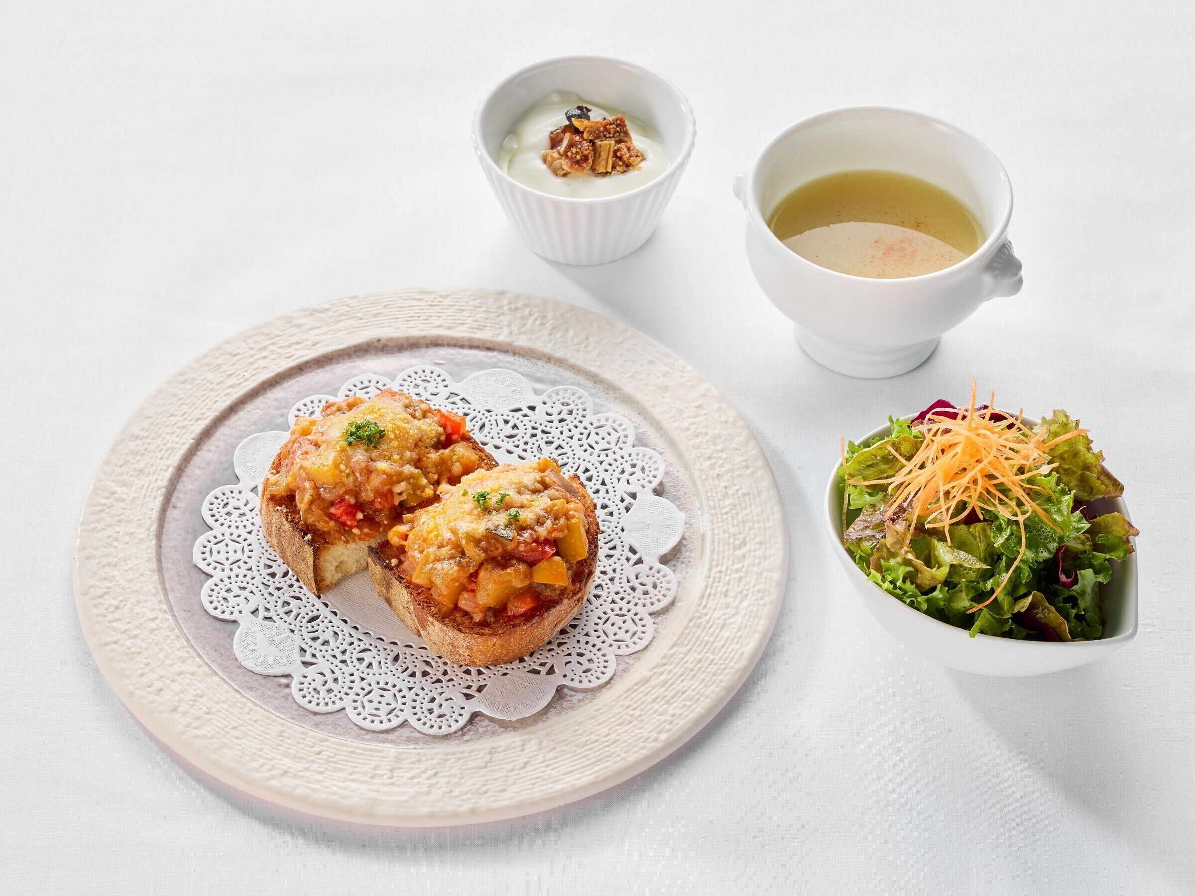 A plate with two open-faced sandwiches topped with a tomato-based spread, a bowl of salad with shredded carrots, and a cup of soup.