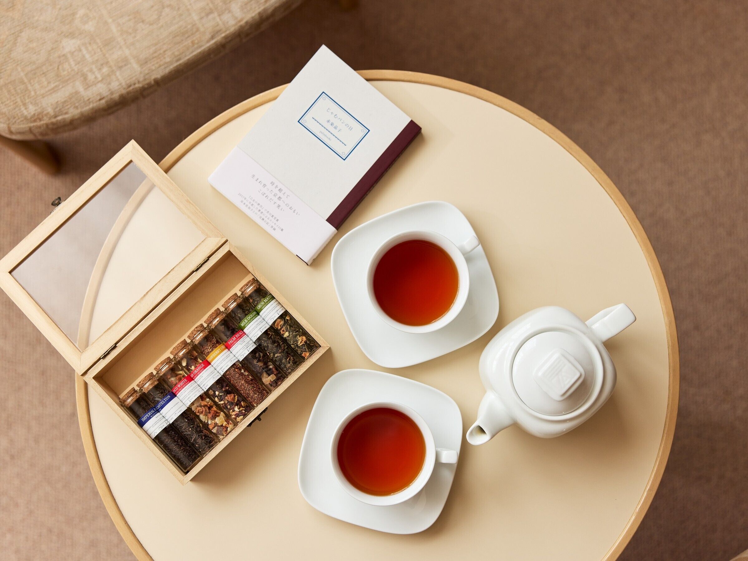 A round wooden tray with two white cups of tea, a teapot, a box of tea bags, and a booklet.