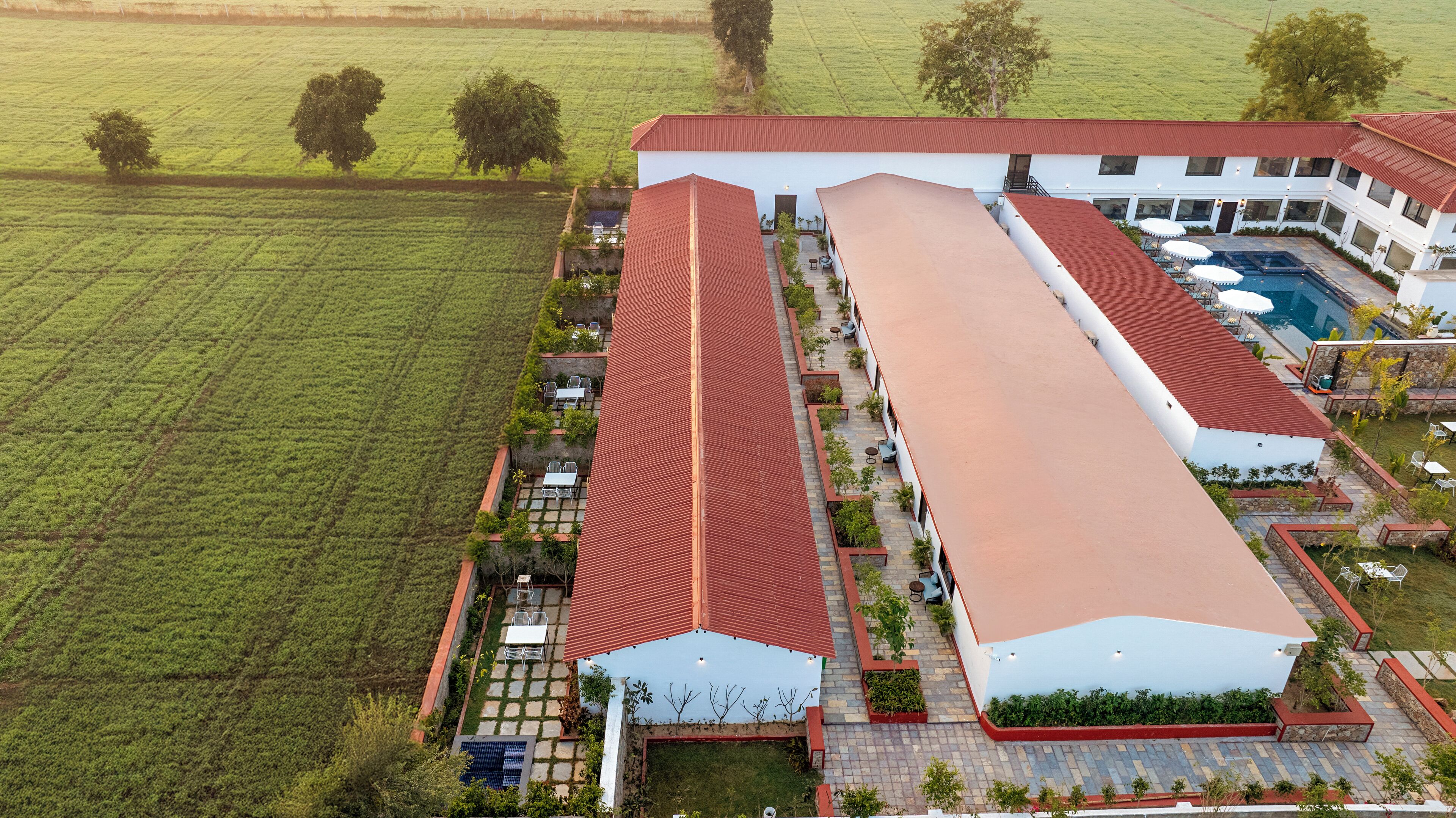 An aerial view of a hotel with a large building, a swimming pool, and surrounding green fields.