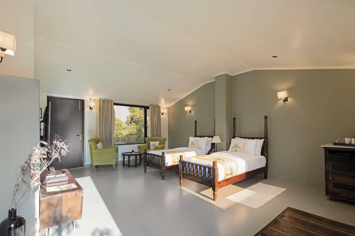 Un dormitorio con dos camas, un sillón verde, una mesita pequeña y un armario de madera.