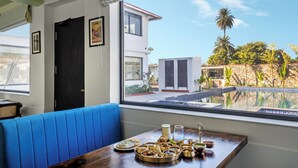 A dining area with a view of a swimming pool, a blue cushioned bench, and a table set with various dishes. - Ratan Villas Jawai (Sumerpur)