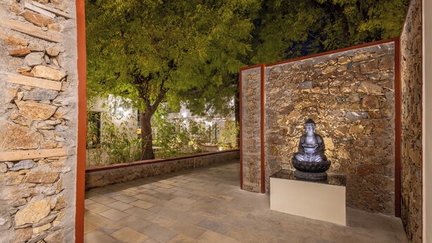 A stone-walled meditation area with a statue, surrounded by trees and a tiled floor. - Ratan Villas Jawai (Sumerpur)