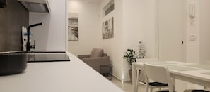 Una cocina moderna con encimera blanca, un fregadero y una zona de comedor con mesa y sillas.