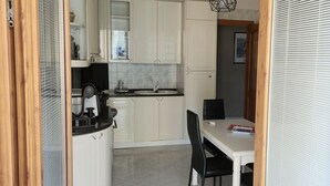 A compact kitchen with white cabinets, a black countertop, and a dining area with a table and chairs. - Dimora Il Roseto - Trani (Trani)