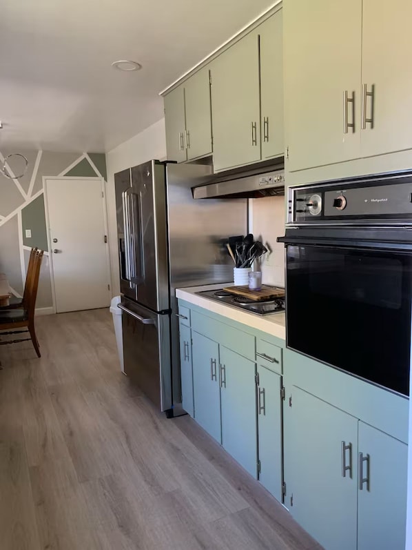 A modern kitchen with light green cabinets, stainless steel appliances, and a black oven.