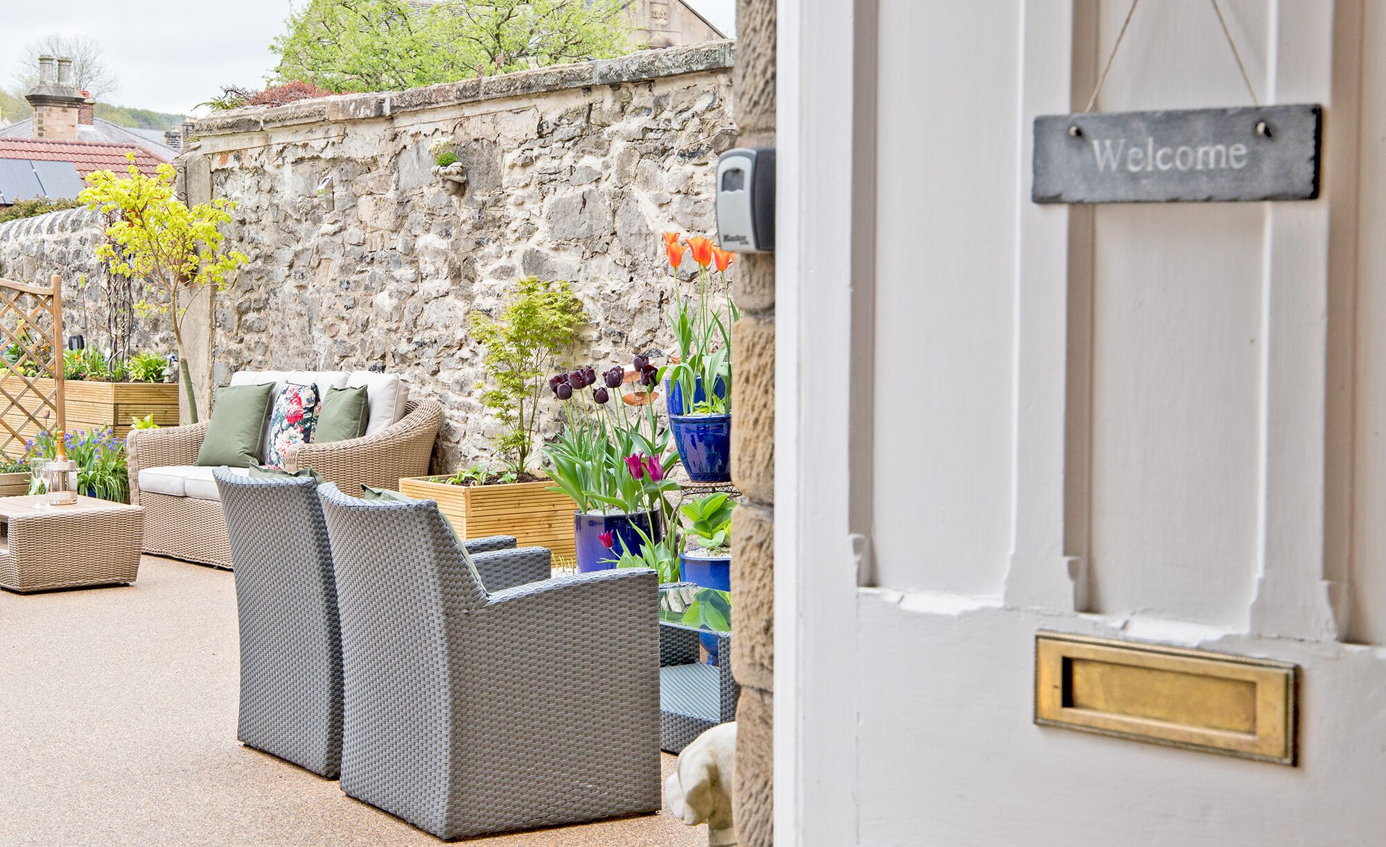 A stone wall with a welcome sign, wicker furniture, and potted plants.