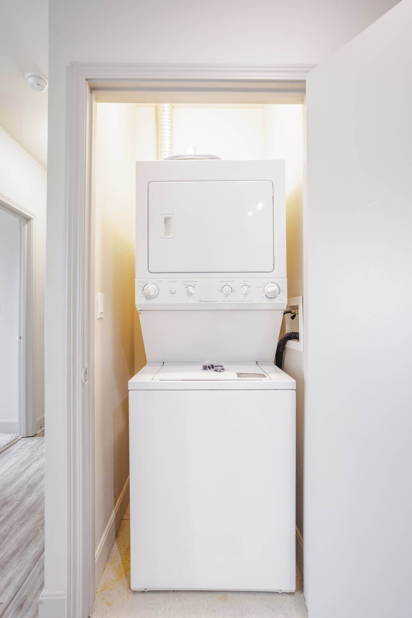 A compact laundry room with a front-loading washer and dryer, a small window, and a door leading to another room.