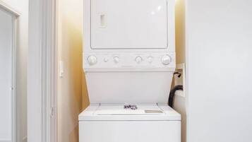 A compact laundry room with a front-loading washer and dryer, a small window, and a door leading to another room.