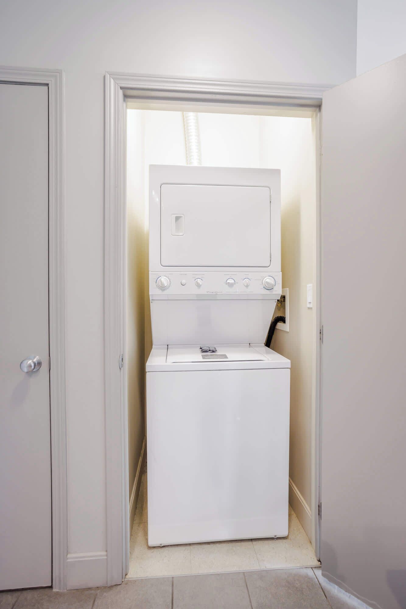 A compact laundry room with a front-loading washer and dryer, a small window, and a door leading to another room.