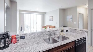 A modern kitchen with granite countertops, a double sink, and a dishwasher. - CozySuites - Current at the Banks (Cincinnati)