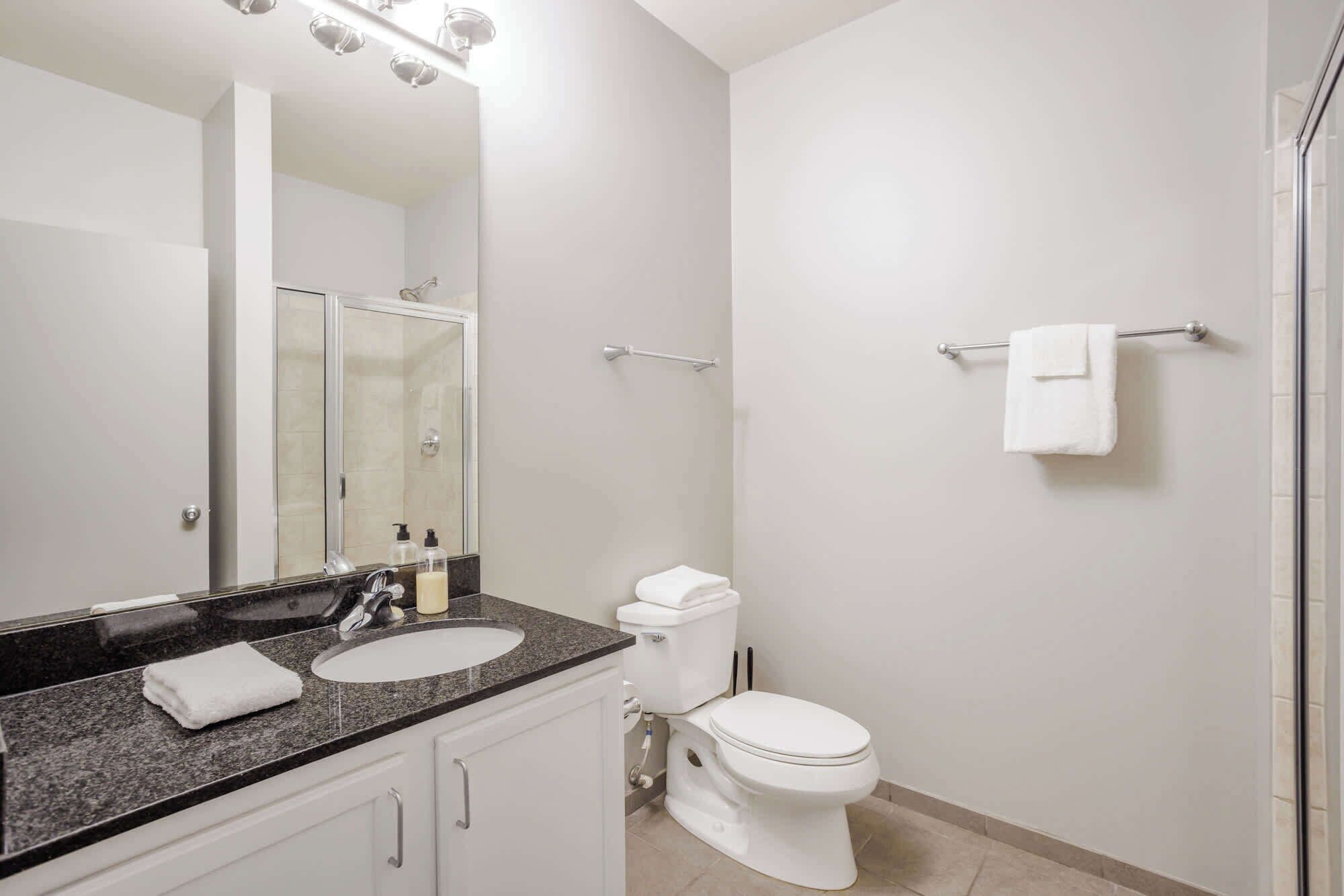 A modern bathroom with a double sink, a toilet, and a glass shower enclosure.