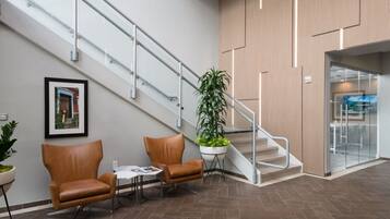 A lobby with a staircase, two leather chairs, a table, a potted plant, and a framed picture on the wall.