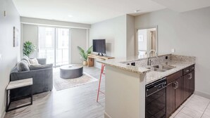 A modern kitchen with granite countertops, a dishwasher, and dark cabinetry. - CozySuites - Current at the Banks (Cincinnati)