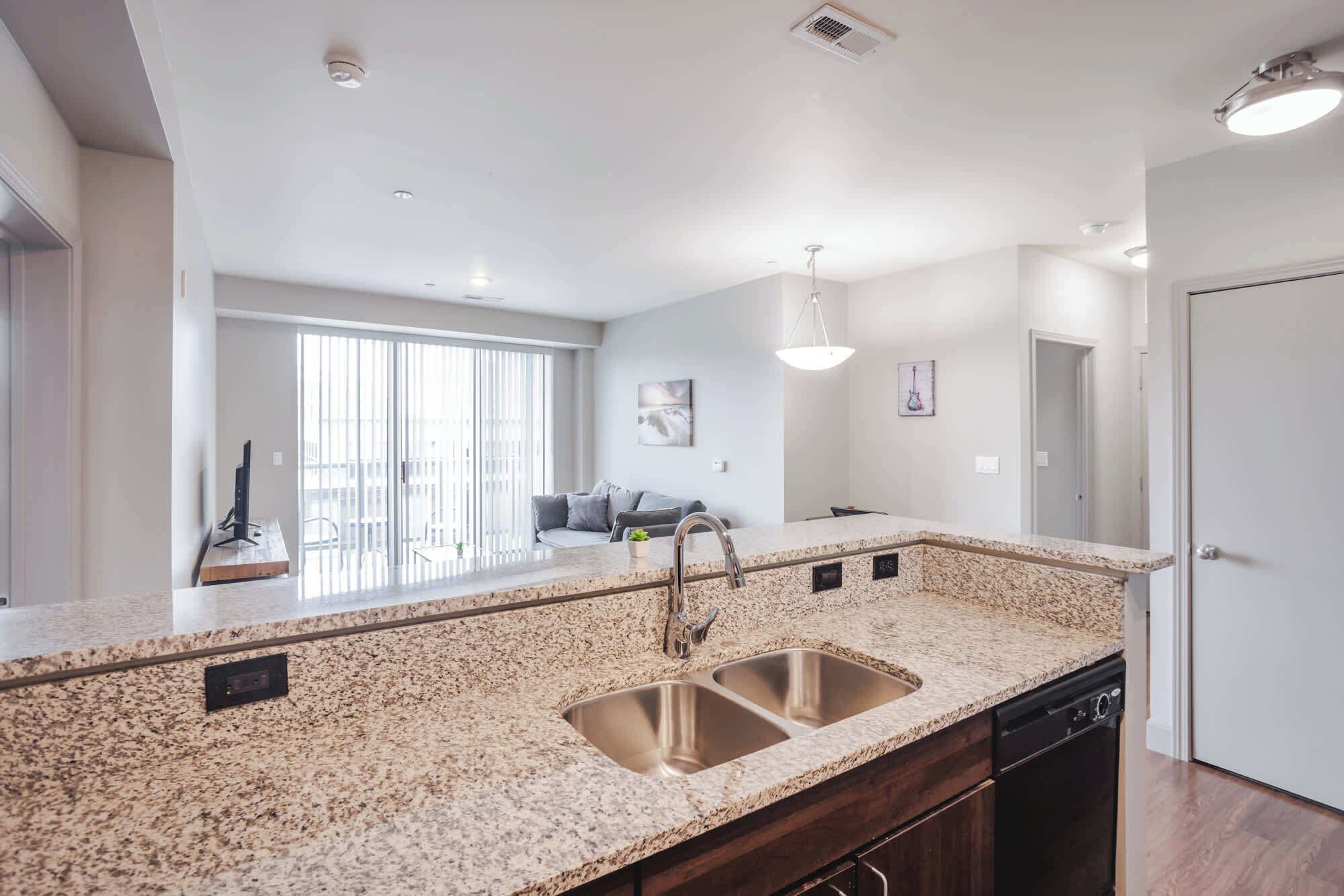 A modern kitchen with granite countertops, stainless steel sink, and built-in dishwasher.