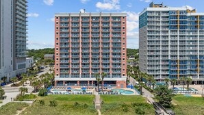 A multi-story hotel with a central courtyard featuring a swimming pool, surrounded by palm trees and lounge chairs. - *Fall into Savings-20% Off New Bookings thru 2026* (Myrtle Beach)