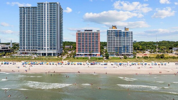 A beachfront hotel with multiple high-rise buildings, a sandy beach, and a clear sky. - *Fall into Savings-20% Off New Bookings thru 2026* (Myrtle Beach)