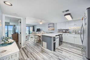 Una cocina moderna con una isla de mármol, armarios blancos y vistas al exterior.