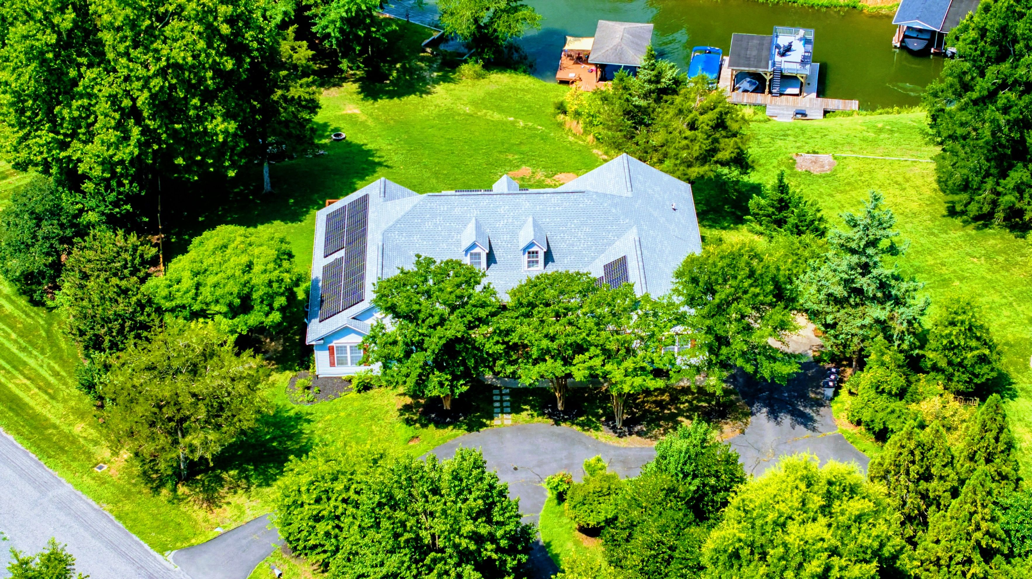 A large house with a sloped roof, surrounded by lush greenery and a pond.