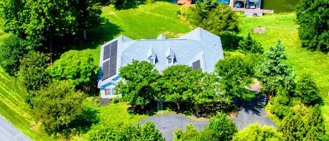 A large house with a sloped roof, surrounded by lush greenery and a pond.