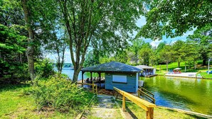A lakeside cabin with a dock, surrounded by lush greenery and trees.
