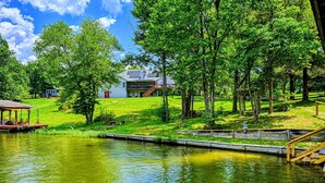 A lakeside property with a dock, a covered seating area, and a house with solar panels.