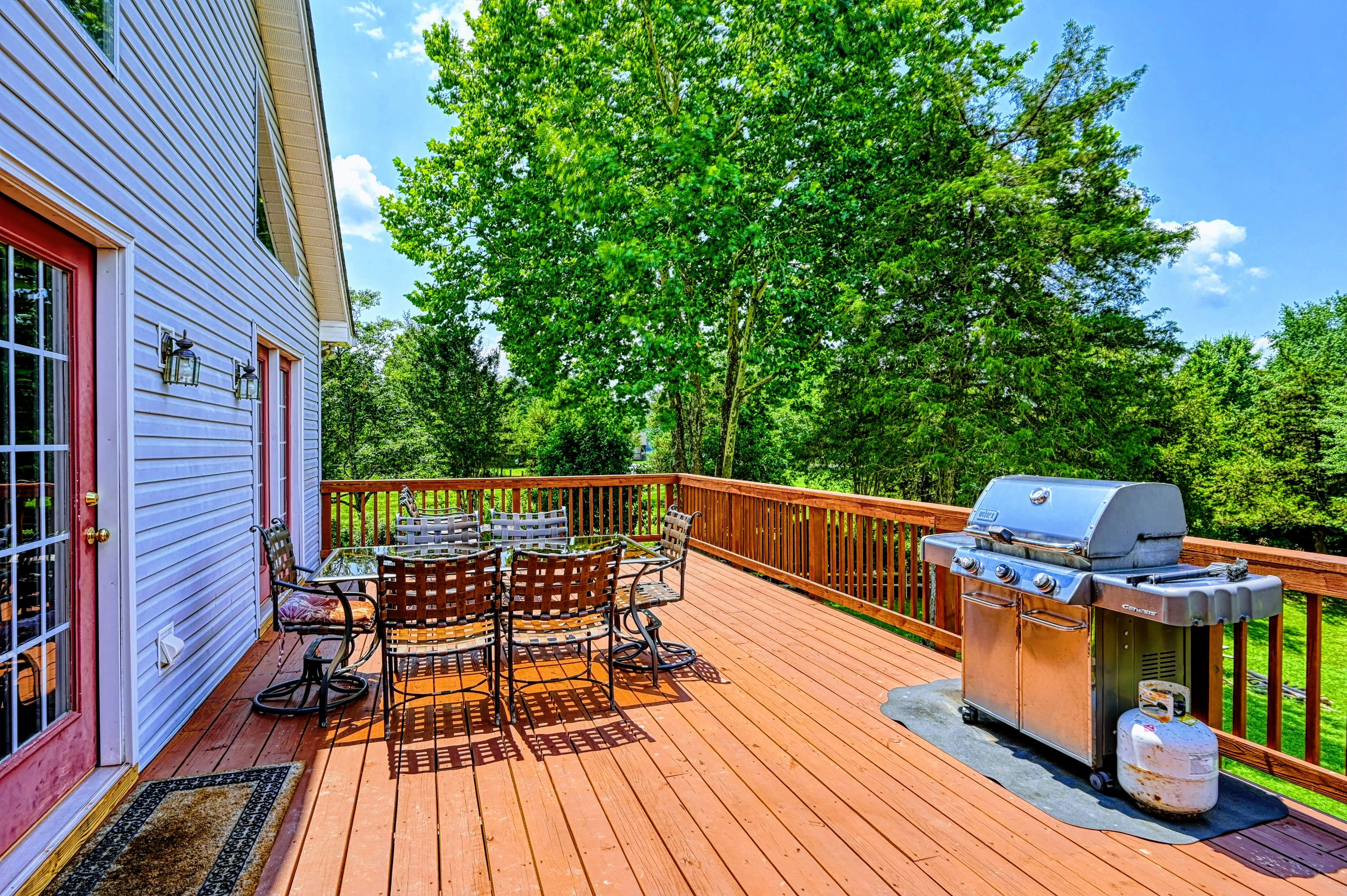 Deck - Upper-level wood deck with a round dining table, chairs, and stainless steel gas grill under the tree canopy.
