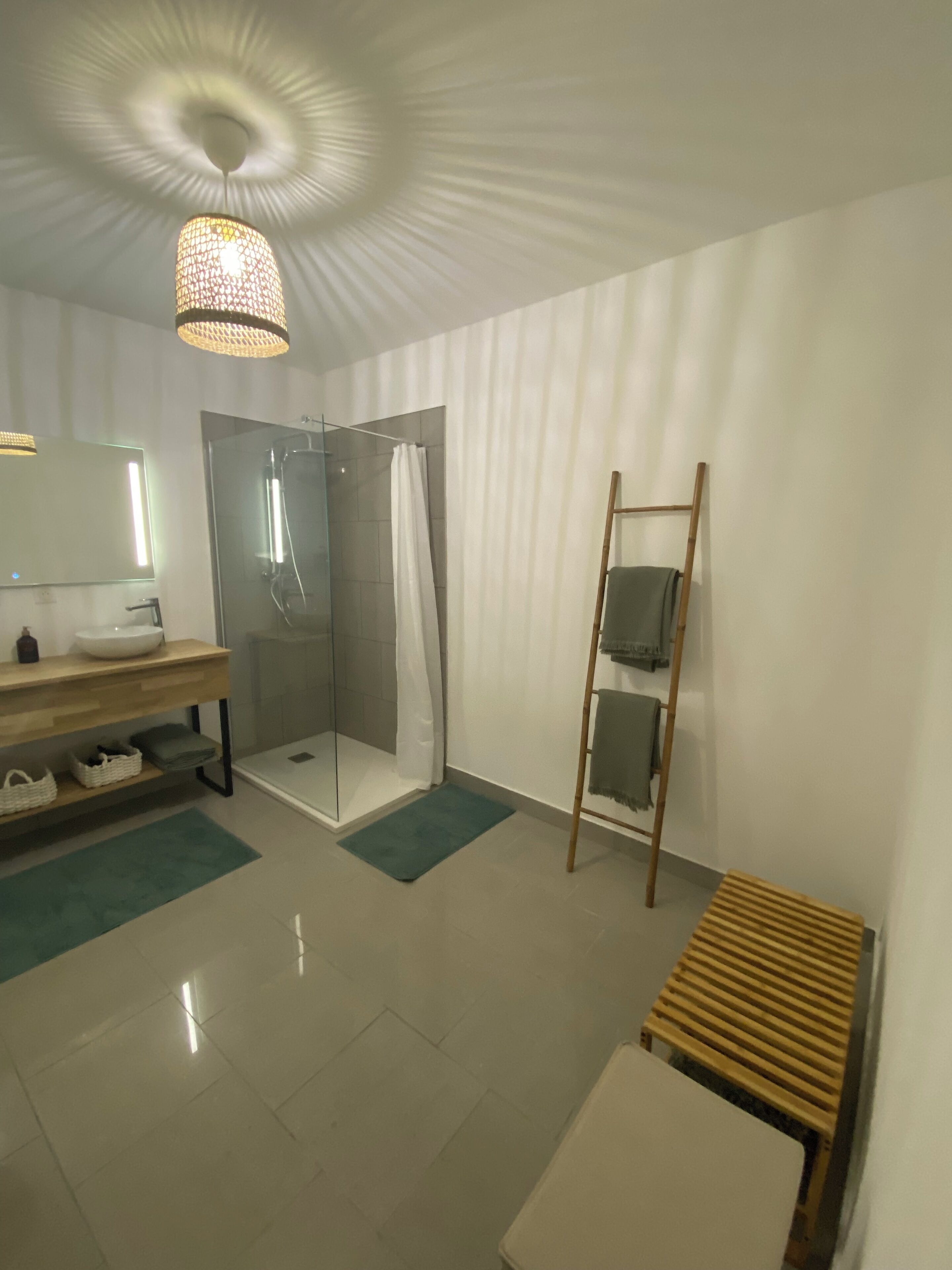 A modern bathroom with a glass shower, a wooden bench, and a hanging light fixture.