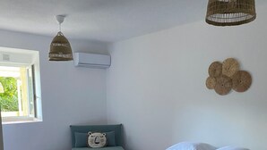 Un dormitorio con una cama, una ventana, aire acondicionado instalado en la pared y una lámpara colgante.