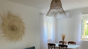 Una sala de estar con un sofá color turquesa, una mesa de centro redonda, un tapete tejido, una mesa de comedor con sillas y una lámpara colgante.