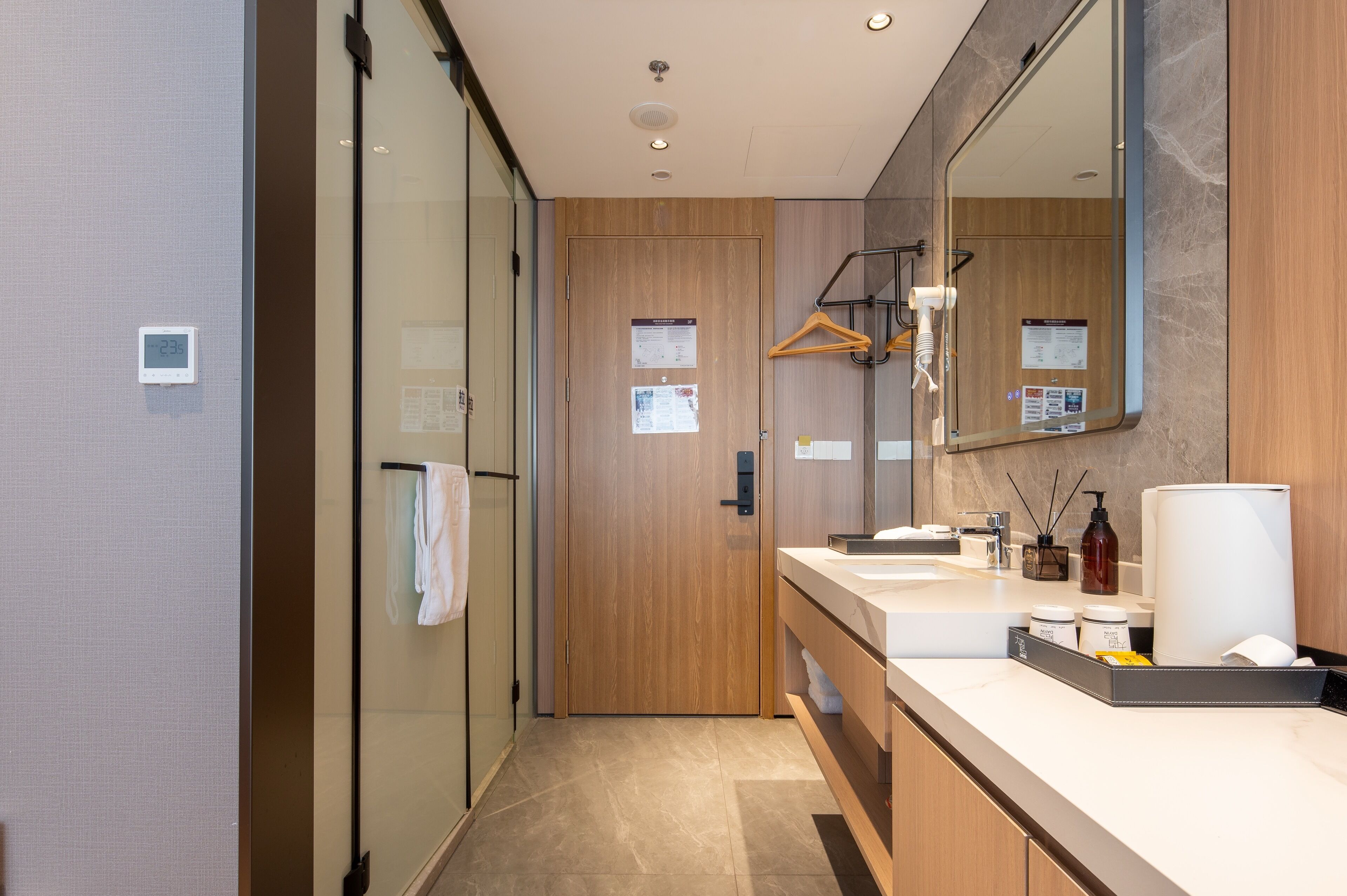 A modern bathroom with a wooden door, a large mirror, and a dual sink vanity.