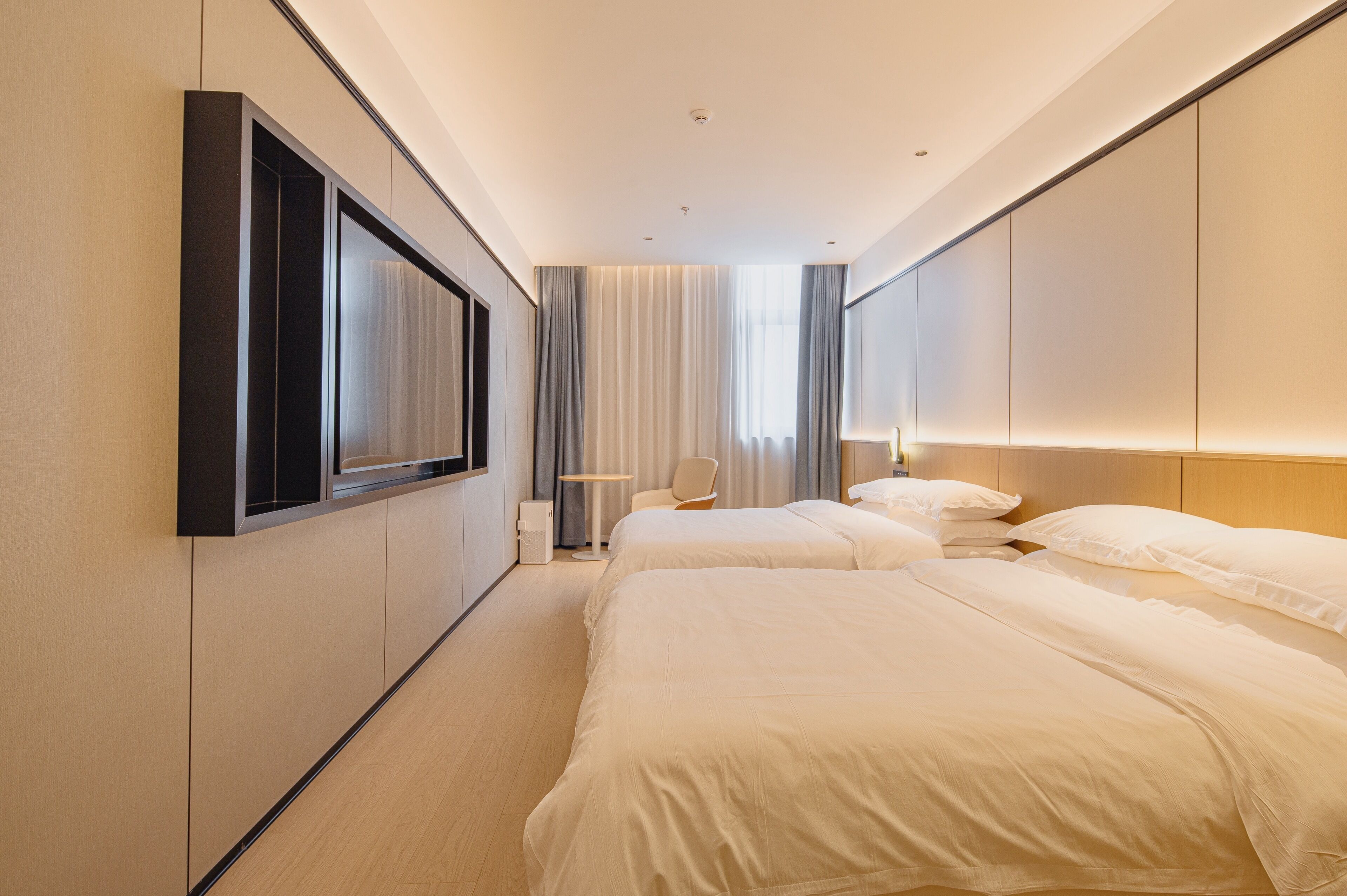A modern hotel room with two beds, a desk, and a large window with curtains.