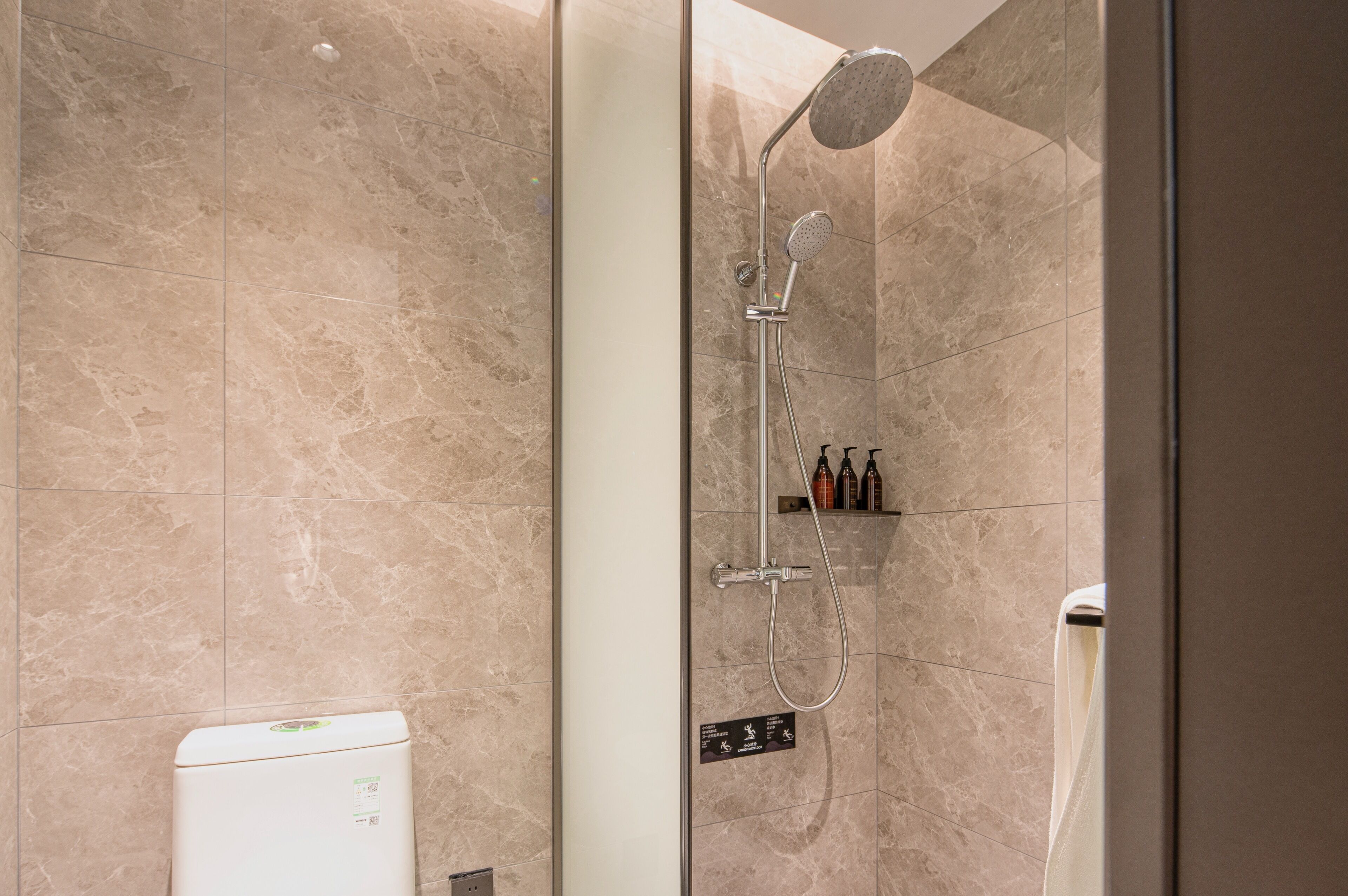 Une salle de bain moderne avec une douche à parois de verre, des carreaux de marbre beige et des toilettes blanches.
