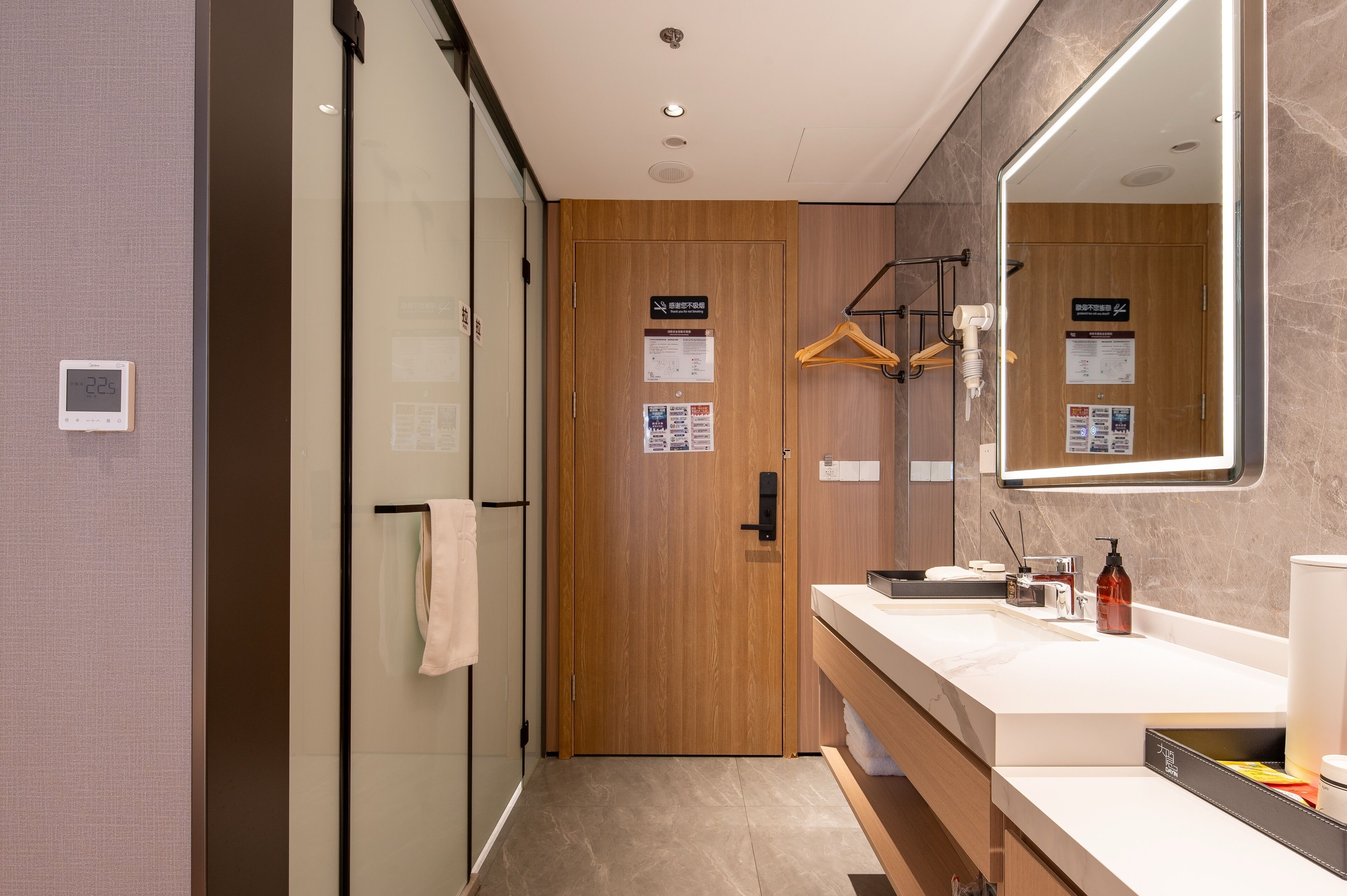 A modern bathroom with a wooden door, a large mirror, a white sink, and a towel rack.