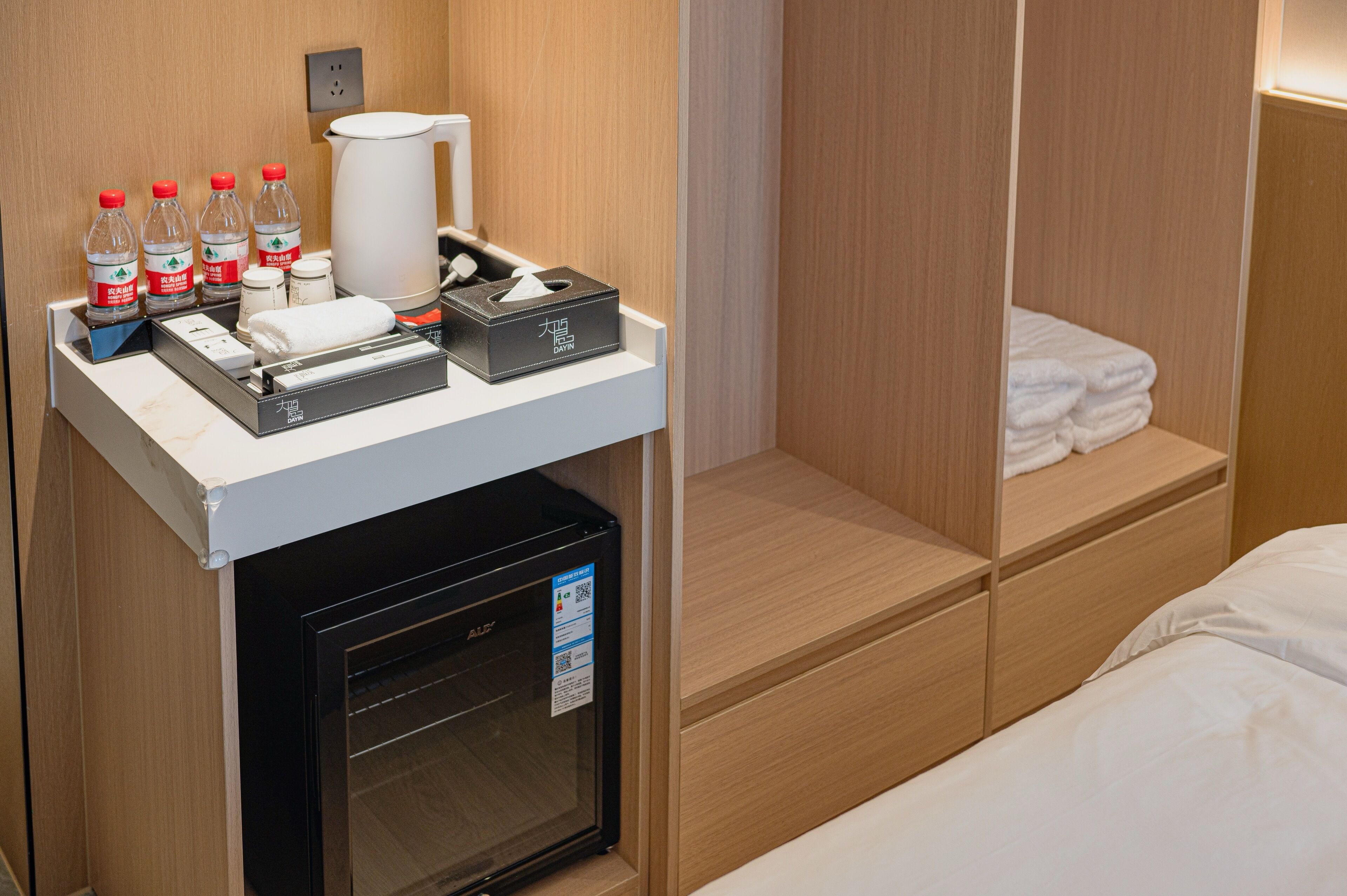 Ett hotellrum med en minibar, en kaffebryggare, flaskvatten, en ask med pappersnäsdukar och prydligt hopvikta handdukar.