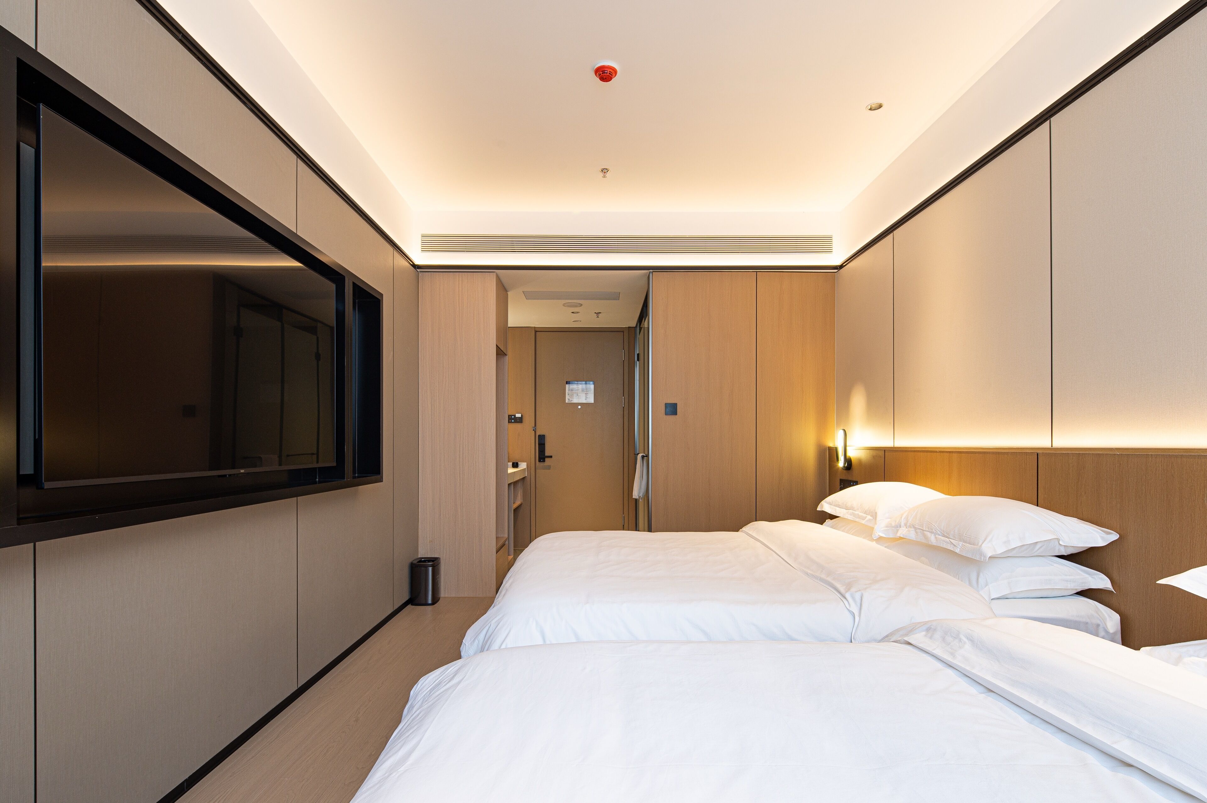 A hotel room with a large bed, a TV mounted on the wall, and a wooden headboard.