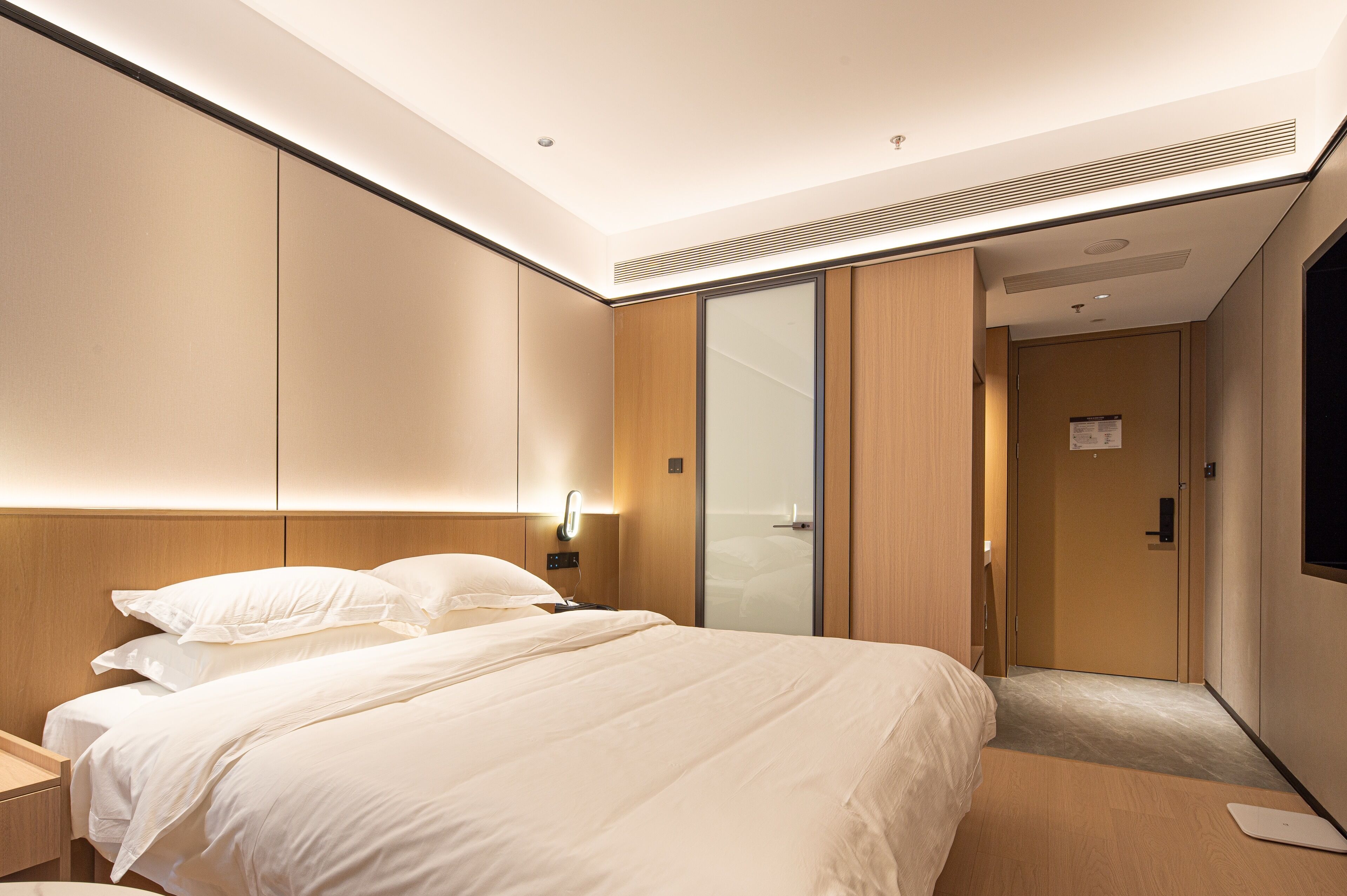 Ein modernes Hotelzimmer mit einem großen Bett, Nachttischen, einem Kleiderschrank und einer Schiebetür zum Badezimmer.