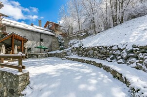 Un'area esterna innevata con un muro di pietra, un pontile in legno e un edificio con facciata in pietra.