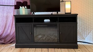 A black entertainment center with a flat-screen TV, a small shelf with toiletries, and a lit candle on top.