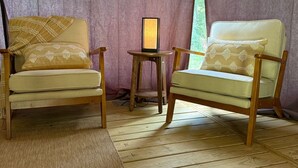 Two wooden chairs with cushions, a small table, and a window with a view of greenery.