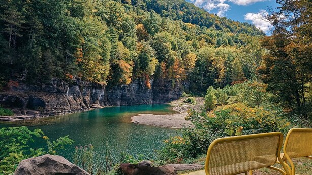 A natural landscape with a lake, rocky cliffs, and a bench.
