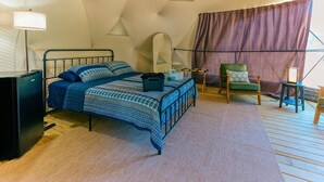 A bedroom with a bed, a chair, a small table, a lamp, and a mirror.