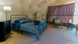 Un dormitorio con cama, mesita de noche, lámpara, silla y una pequeña mesa con espejo.