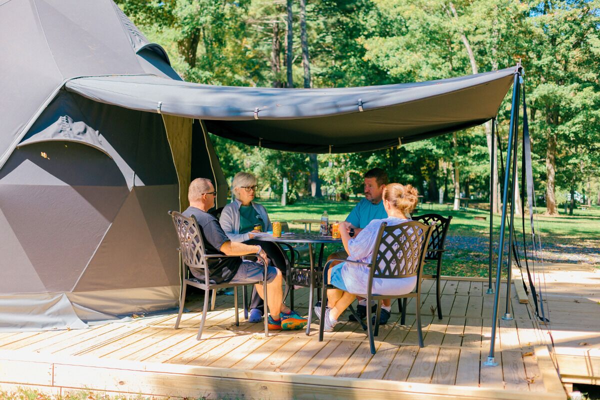 A group of people seated at a table under a canopy, with a tent in the background.