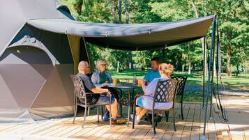 A group of people seated at a table under a canopy, with a tent in the background.