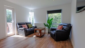 A modern living room with two black leather sofas, a wooden coffee table, and a large green plant.