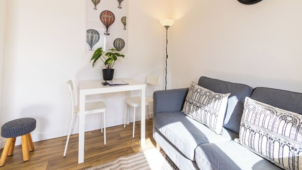 Ein modernes Wohnzimmer mit einem weißen Esstisch, einem grauen Sofa und einer Wanduhr.